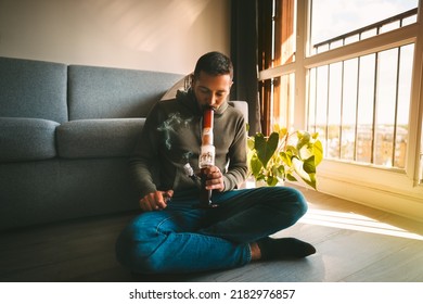 Man Smoking Bong And Inhaling The Smoke At Home. Man Smoking Pot, Medical Marijuana Or Cannabis From A Bong Or Water Pipe