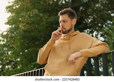 Man smoking cigarette near railing outdoors. Bad habit - Powered by Shutterstock