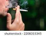 Man smoking cigarette at summer day,closeup.Blurred outdoors green background.Copy space.