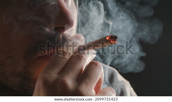 Man smoking a marijuana weed joint, inhaling\
cannabis smoke.