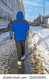 A Man In Sneakers Walks Along The Sidewalk Covered With Melting Snow