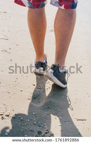 a man in sneakers walks on the sand near the sea


