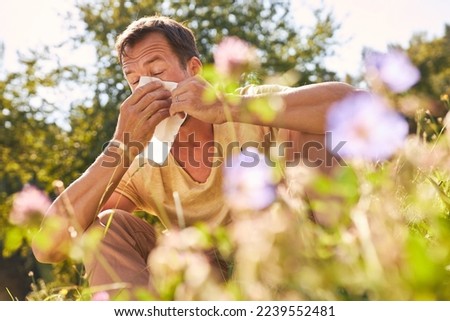 Man sneezing into handkerchief with hay fever in a blooming summer meadow