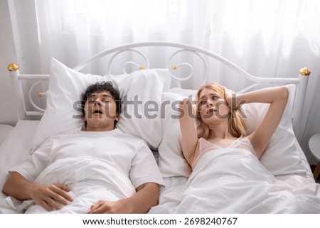 A man snores loudly in bed, causing his wife to lose sleep and become irritated. Couple snores.