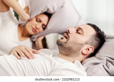 A man snoring and sleeping in the bed while woman is annoyed of it. - Powered by Shutterstock