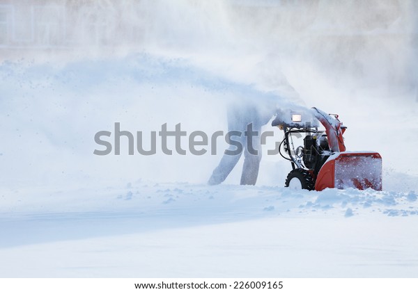 man\
with a snow blowing machine working in winter\
day