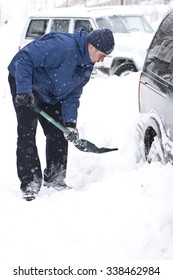 Man With A Snow Shovel. Car And Street Under Snow.