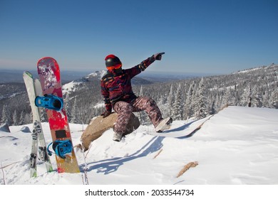 A Man In Snowboarding Gear On The Top Of A Mountain. Young Man Standing With A Snowboard On The Top Of The Mountains