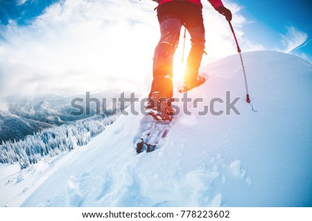 A man in snowshoes in the mountains in the winter. A climber with trekking sticks walks through the snow. Winter ascent. Beautiful sky with clouds.