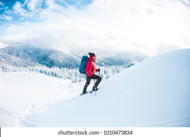 A man in snowshoes and trekking sticks in the mountains. Winter trip. Climbing of a climber against a beautiful sky with clouds. Active lifestyle. Climbing the mountain through the snow. - Shutterstock ID 1010473834