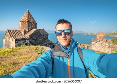 Man Solo Traveler Takes Selfie Photo Against The Background Of Sevanavank Monastery At The Sevan Lake. Vacation In Armenia Concept