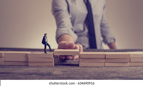Man Solving Problems By Building Bridge With Wooden Block To Span A Gap For Little Businessman Walking Across In A Conceptual Retro Toned Image.