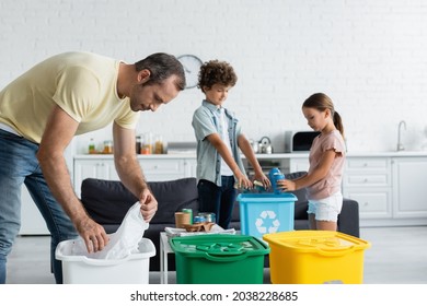 Man sorting garbage near blurred kids and trash cans with recycle sign at home - Shutterstock ID 2038228685