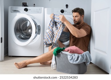 A man sorts clothes in the laundry room, focusing on a plaid shirt next to a washing machine in a small, tidy space - Powered by Shutterstock