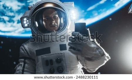 Man in a Space Suit Casually Talking on a Phone in Outer Space While Holding on to a Satellite. Astronaut Chatting with Mission Control Crew, Family or Work Colleagues on a Video Call on a Smartphone