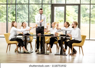 Man speaking toast during a business lunch with colleagues sitting at the spacious restaurant with big window on the background - Powered by Shutterstock