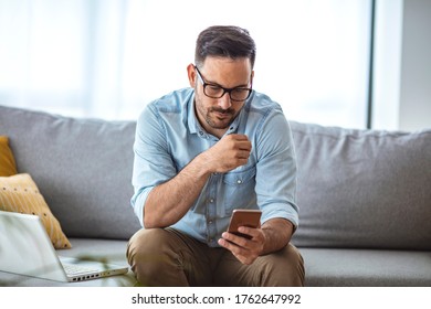 Man With Spectacles Relaxing Sitting On Couch While Looking At Mobile Phone. Closeup Of Mature Man Using Smartphone To Checking Email At Home. Man Reading Email On Smartphone