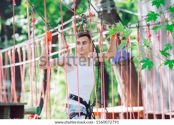 Man spend their leisure time in a ropes course. Man
engaged in rope park.