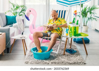 Man spending his summer vacations at home, he is sitting on a deckchair in the living room and reading a book