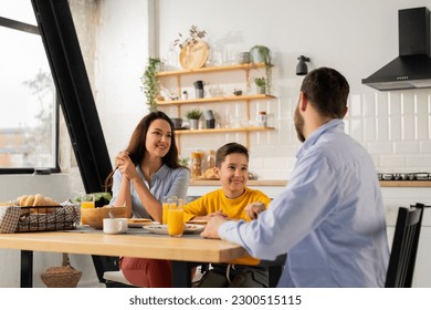 A man spends time with his family during a family breakfast. A friendly family sits at the kitchen table and eats sandwiches with orange juice for breakfast. - Powered by Shutterstock