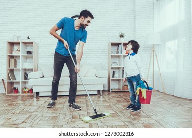 Man Spends Time With His Son. Father Of Boy Is Engaged In Raising Child. Father Is Teaching A Son A Cleaning. Father And Son Washing The Floor With Mop. People Is Located In Bedroom.