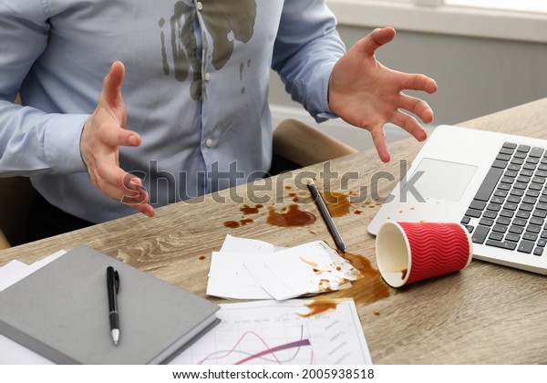 Man with spilled coffee over his workplace and\
shirt, closeup