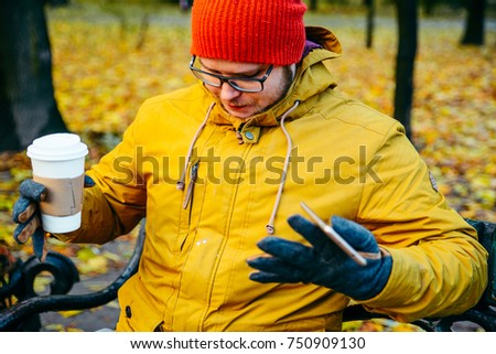 Man is spilling coffee on his jacket outside in autumn park