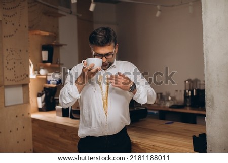 Man is spilling coffee on white shirt while drinking in office.
