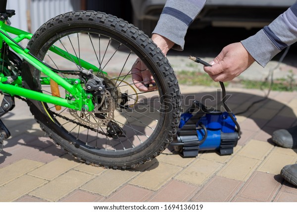 man spins a nipple on the wheel of a children\'s\
bicycle, after pumping a flat tire with a compressor. Home\
maintenance of bike.\
close-up