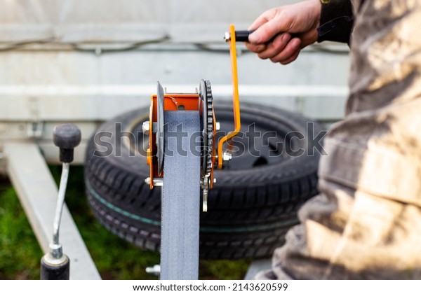 A man spins the winch handle on a\
car trailer. Towing and transportation of special equipment,\
loading and unloading of cargo. selective\
focus