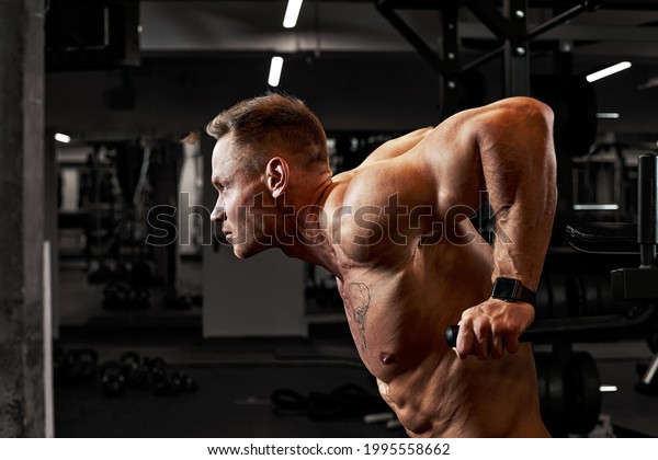 A man with sports\
aggression doing press on the uneven bars in a gym, training\
pectoral muscles and triceps