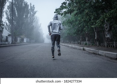 Man in sportswear runs down the road on a foggy morning. View from the back Sports workout marathon.