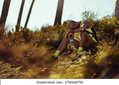 Man in sportswear sitting on the group and relaxing after trail run training. Male trail runner taking break after running workout on mountain path. - Powered by Shutterstock