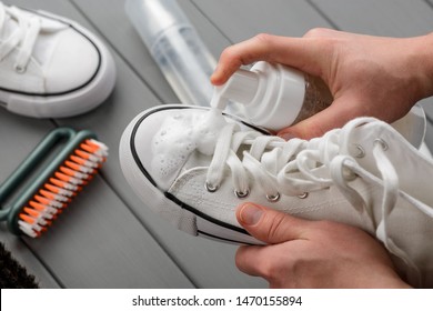 Man Spraying Cleaner Foam Onto A White Sneaker, Closeup Shot. Proper Care For Canvas Footwear.