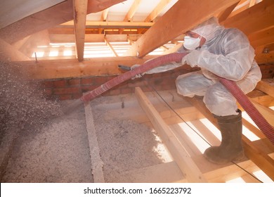 A man is spraying ecowool insulation in the attic of a house. Insulation of the attic or floor in the house