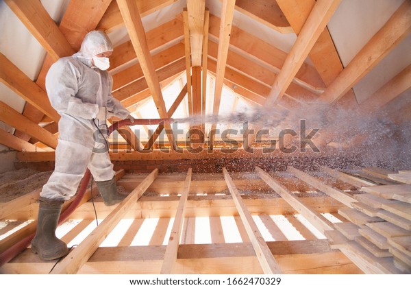 A man is\
spraying ecowool insulation in the attic of a house. Insulation of\
the attic or floor in the\
house