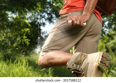 Man Spraying Tick Repellent On Leg During Hike In Nature, Closeup