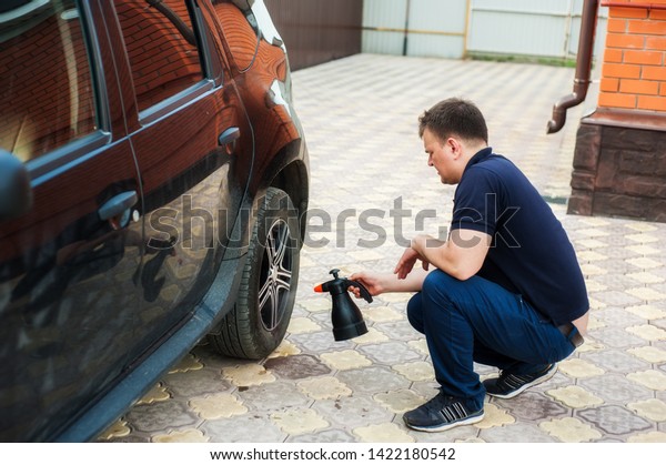 A man sprays car shampoo on a black car from
a plastic bottle. Car wash
concept
