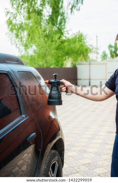 A man sprays car shampoo on a black car from
a plastic bottle. Car wash
concept