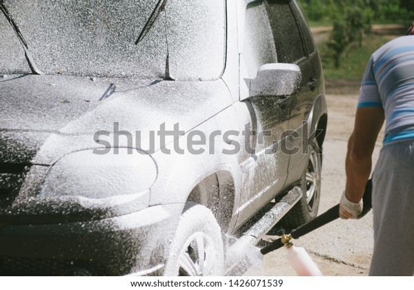 A man sprays a cleaning agent with a high pressure
washer on a car. The car washes with a means of washing. The
machine is in foam