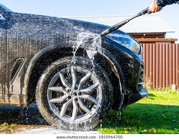 A man sprays foam shampoo on the front\
fender while self-washing a car in the\
yard