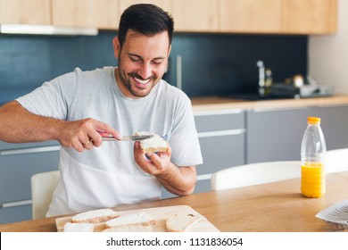 Man Spreading Cream Cheese On Baguette Slice On Wood Board