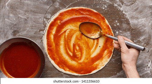 Man Spreading Tomato Sauce On Raw Pizza Base, Top View