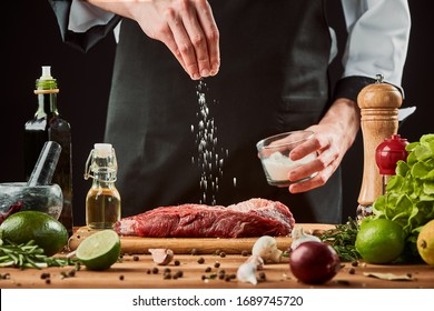 Man sprinkles salt over meat. Chef cooking a beef steak, seasoning with pepper, lime, olive oil, garlic and onion.
