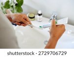 Man squeezing out toothpaste onto toothbrush before brushing. Hands gripping toothpaste tube and brush while preparing for morning routine. Man preparing for dental care routine.