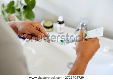 Man squeezing out toothpaste onto toothbrush before brushing. Hands gripping toothpaste tube and brush while preparing for morning routine. Man preparing for dental care routine.