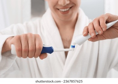 Man squeezing toothpaste from tube onto electric toothbrush indoors, closeup - Powered by Shutterstock