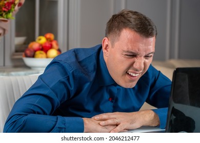 Man Squints And Tries See Something Small Or Reading Suspicious Message On Laptop Screen In Living Room At Home. Confused Millennial Man Reading News On Laptop With Disgust, Unpleasant Negative Emotio