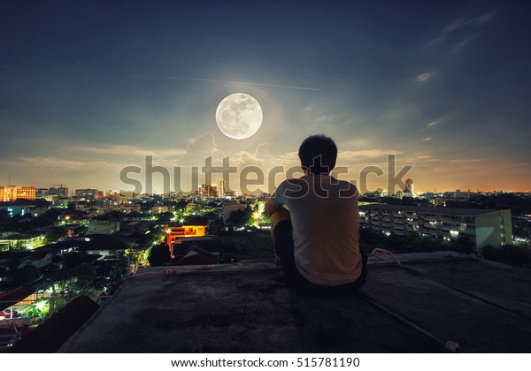 A man stand alone watch the full Moon night in\
the Bangkok city, Thailand.