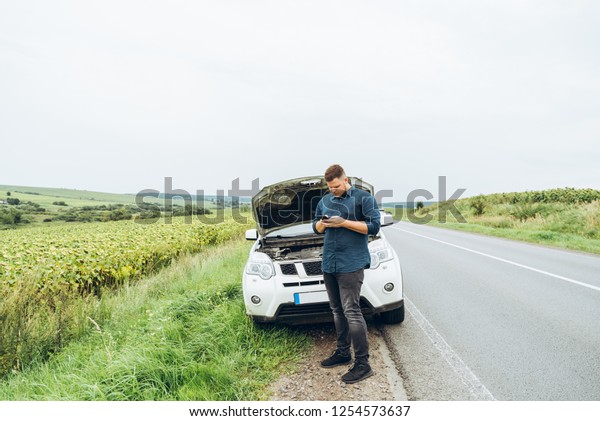 man stand in front of broken car with phone.
broken in the middle of
nowhere